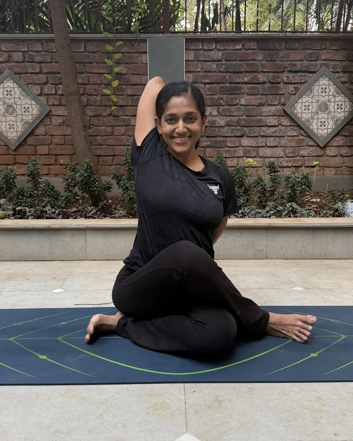 Rashmi Ramesh, creator of Yogalates Strength Plus, smiling in a seated yoga twist on her mat